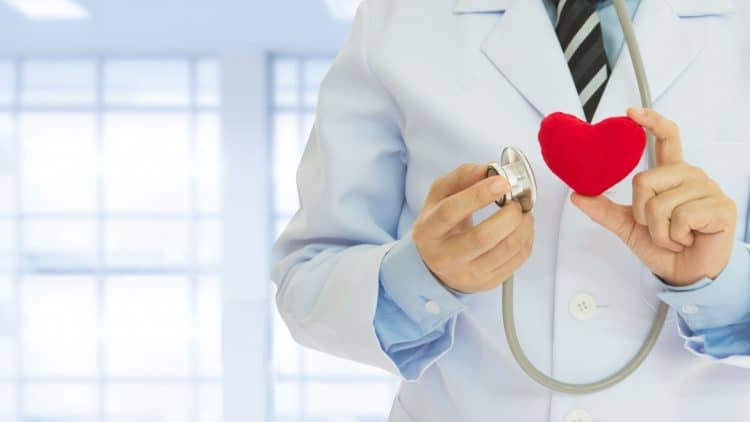 male doctor holds up heart plushie and stethoscope