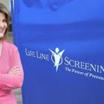 Nurse Barb in a pink sweater next to a Life Line Screening Divider in blue